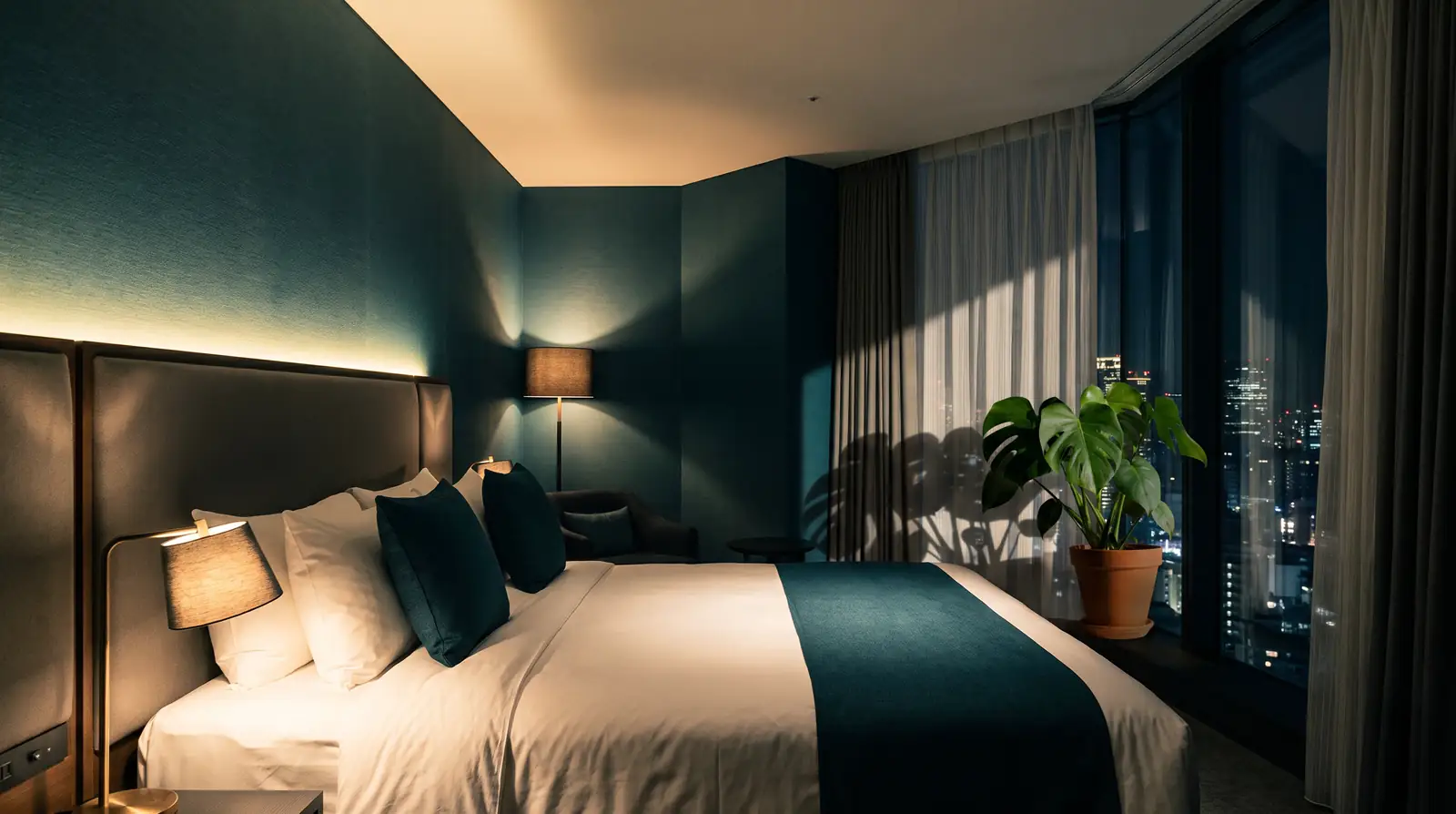 A hotel guest room at night, lighting layered from a bedside lamp, a cove light and a floor lamp
